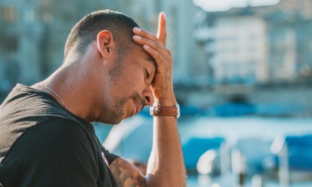 Auf dem Bild ist ein Mann zu sehen, der sich mit der Hand an die Stirn fasst.
