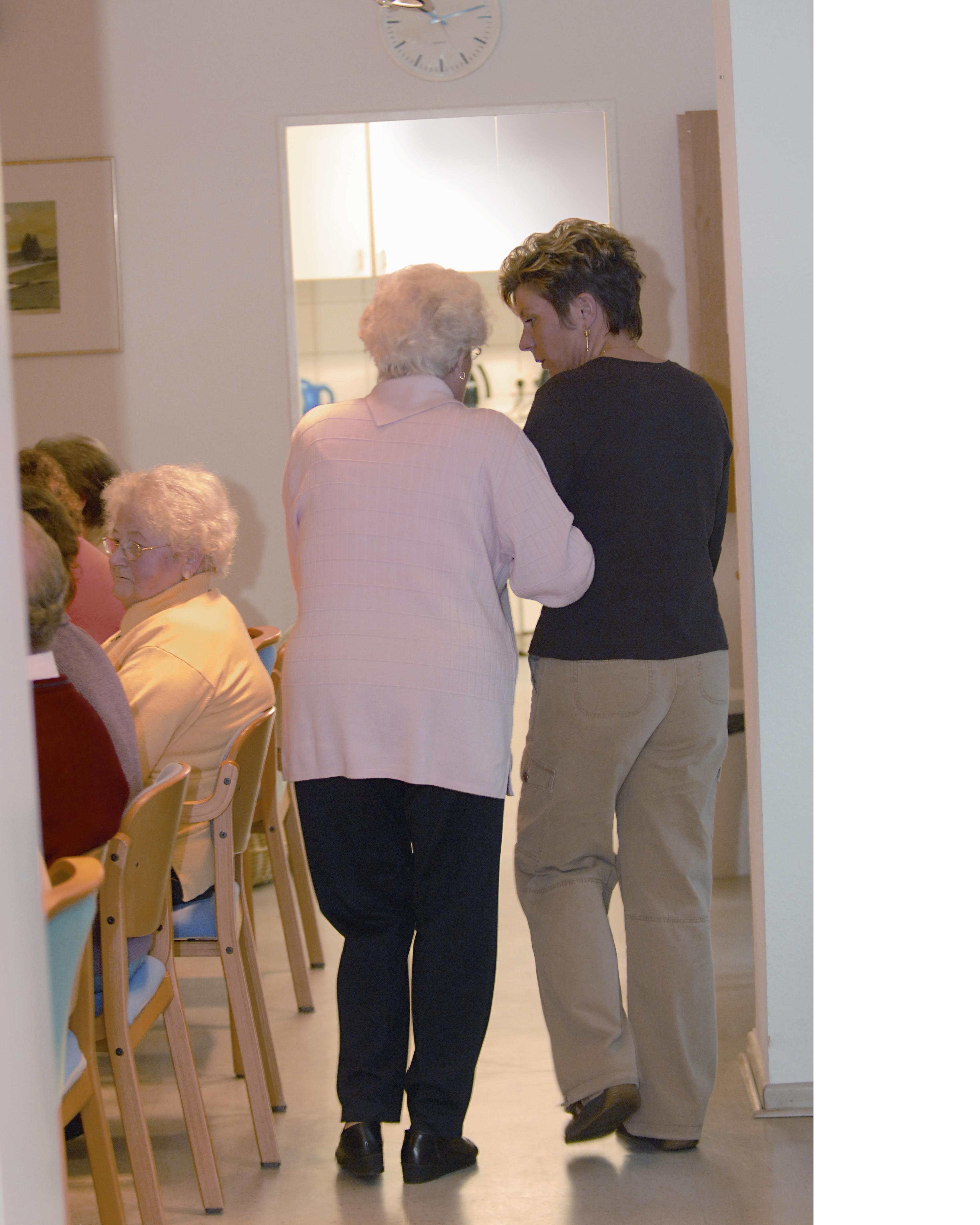 Foto: Krankenschwester, die eine Patientin zum Tisch begleitet.