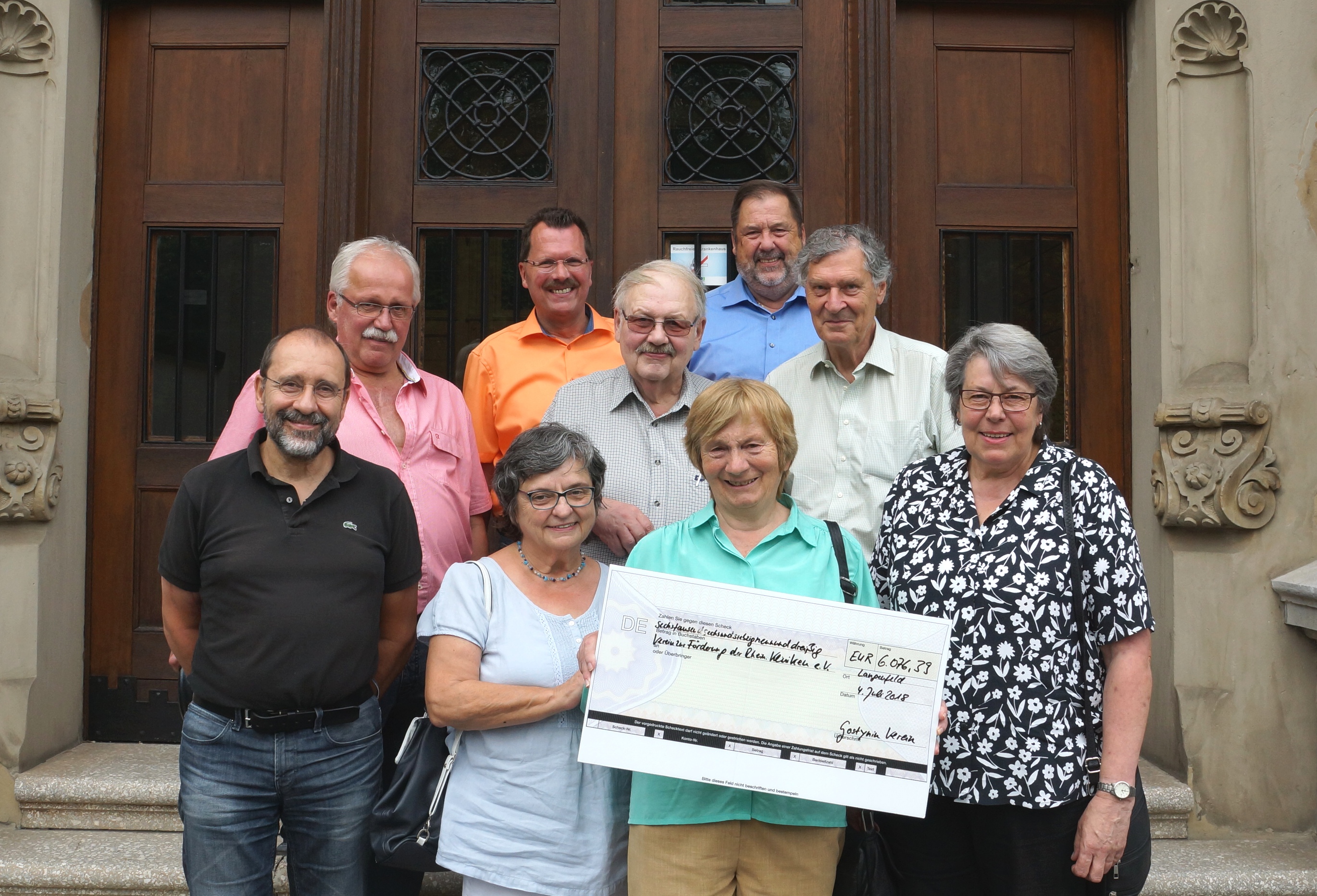 Foto: Personen mit Check vor dem Haupteingang des Verwaltungsgebäudes